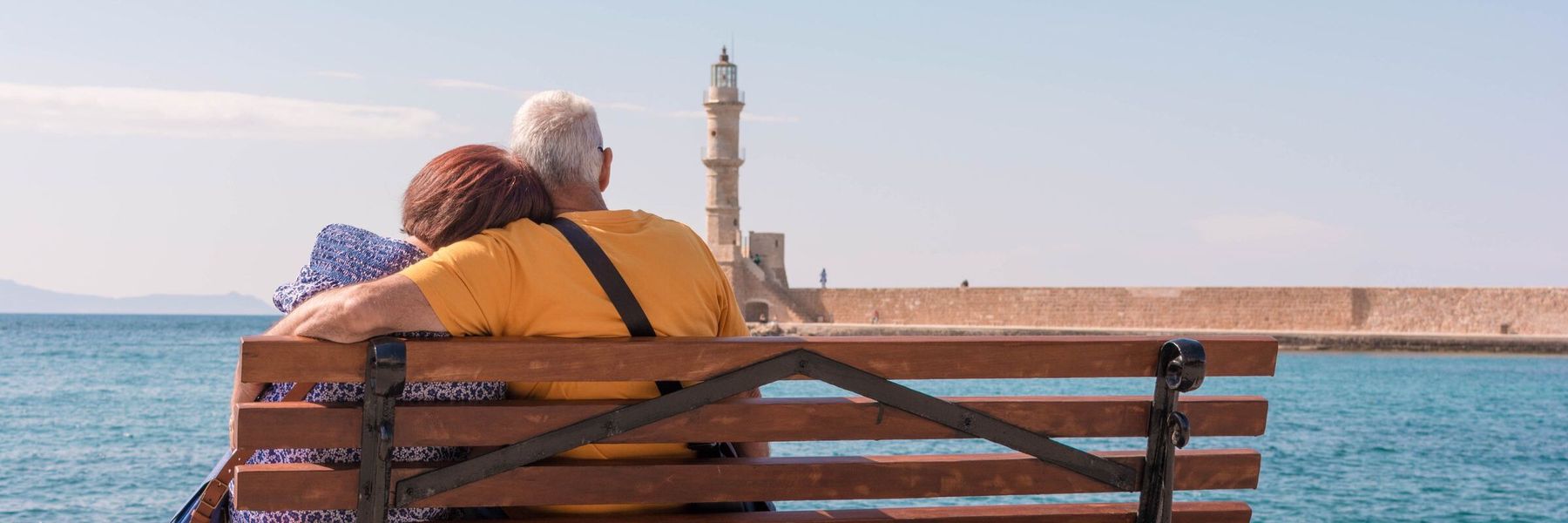 Paar auf einer Bank am Meer, im Hintergrund ein Leuchtturm